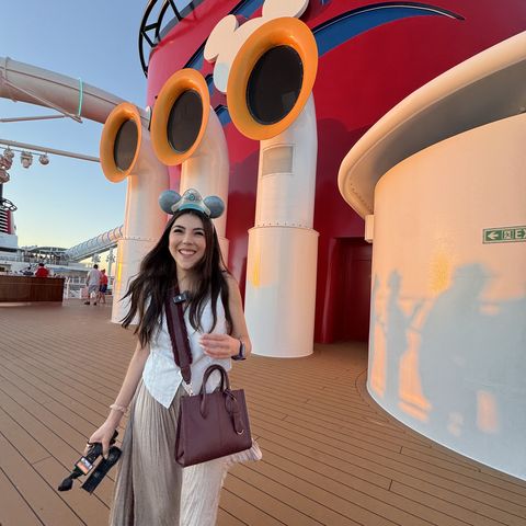 Dani Godinez con orejas de Mickey caminando por la cubierta de un barco de Disney Cruise Line, junto a la chimenea