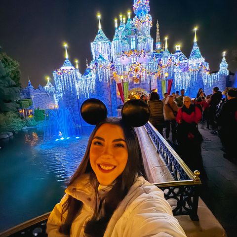 Dani Godinez de noche frente al Castillo de la Bella Durmiente iluminado en Disneyland