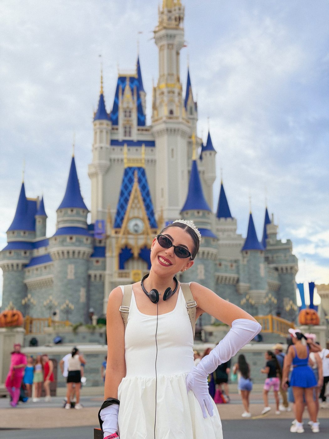 Dani Godinez disfrazada de la princesa de Genovia, con tiara y guantes blancos, frente al Castillo de Cenicienta decorado para Halloween.