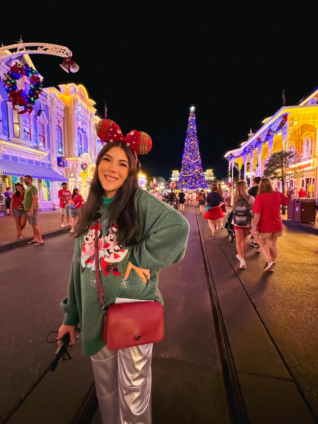 Dani Godinez de noche en Main Street, decorada de Navidad, con el árbol iluminado al fondo.