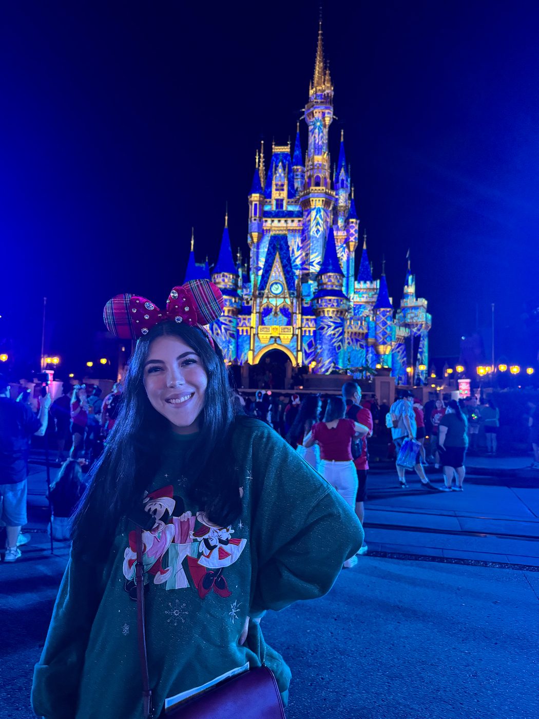 Dani Godinez con orejas navideñas frente al Castillo de Cenicienta iluminado de noche durante la Mickey's Very Merry Christmas Party.