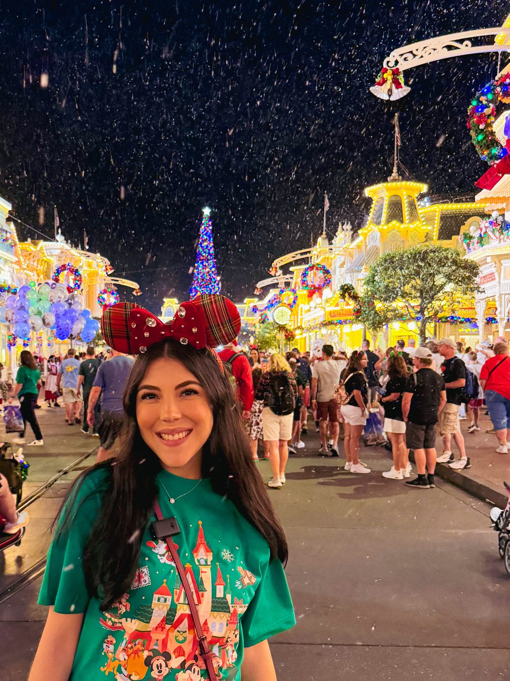 Dani Godinez en Main Street con nieve cayendo y el árbol de Navidad al fondo, en la fiesta de Navidad de Magic Kingdom.